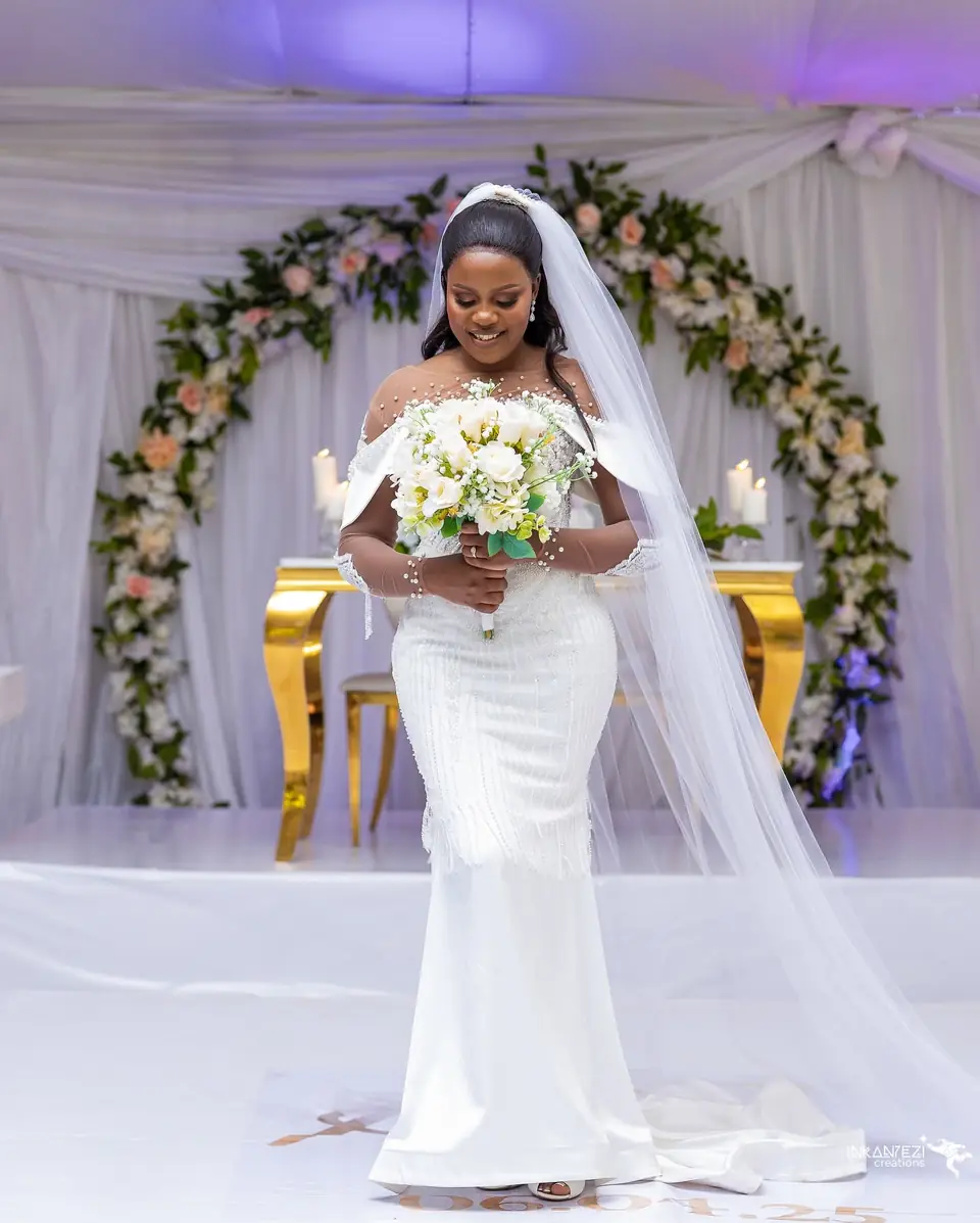 A bride under a floral arch in a beaded mermaid gown and long veil